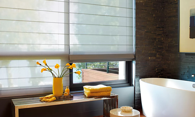 Sunlit bathroom featuring Hunter Douglas window blinds, white wash basin, two yellow towels, and vibrant yellow flowers in a matching vase.